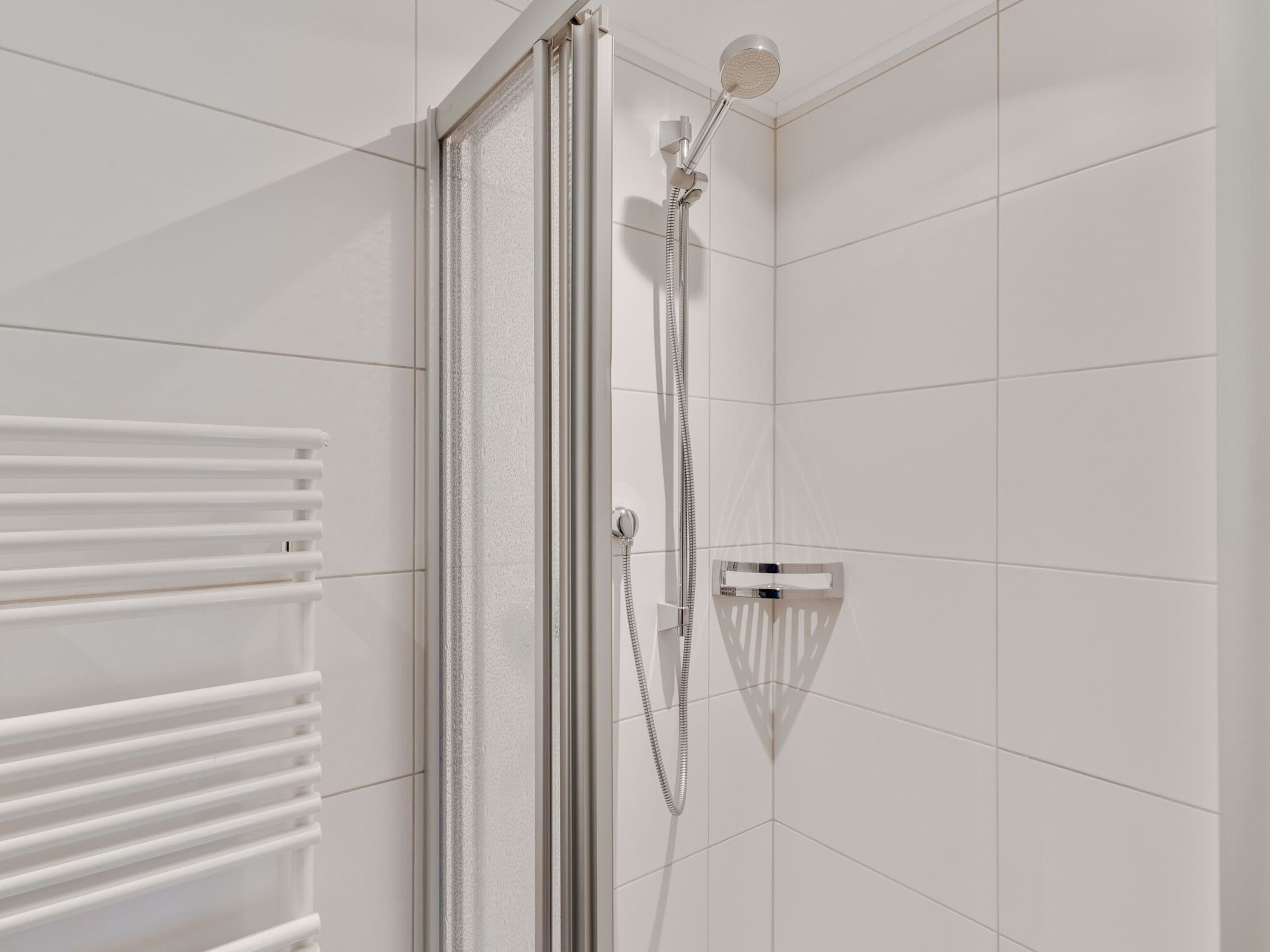 Een moderne douche met een handdouche en een bedieningspaneel aan de muur.