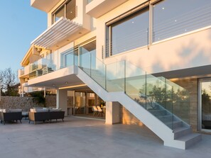 A modern multi-story house with a glass staircase, outdoor seating area, and a stone wall.