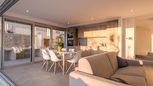 A modern living room with a sofa, a dining table with chairs, and a kitchen area with wooden cabinets and a built-in oven. - Luxurious Villa in Kozino With Fenced Garden (Zadar)