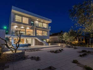 A modern two-story house with a spacious patio, a staircase, and a well-lit outdoor area.