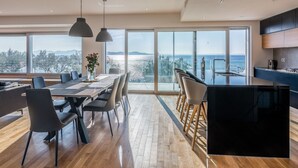 A modern kitchen with a large island, dining area with chairs, and large windows offering a view of the sea. - Luxurious Villa in Kozino With Fenced Garden (Zadar)