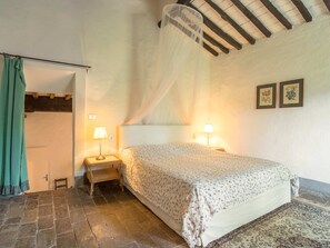A bedroom with a bed, two bedside lamps, a nightstand, a woven chair, a curtain, and a patterned rug. - Rustic Farmhouse Stay, Carmignano (Carmignano)