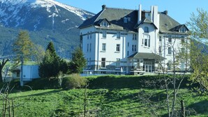 A large, white building with multiple windows and a prominent chimney, surrounded by green grass and trees, with a mountain in the background. - Chalet With Garden in the Pyrenees (Roquefort-de-Sault)