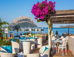 Relax on the deck overlooking the marina, surrounded by boats and a scenic rocky hill.
