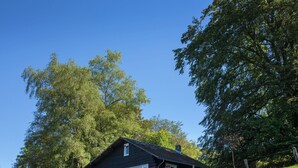 Une cabane en bois rustique, dotée d’un toit en pente, entourée d’une végétation luxuriante et d’arbres.