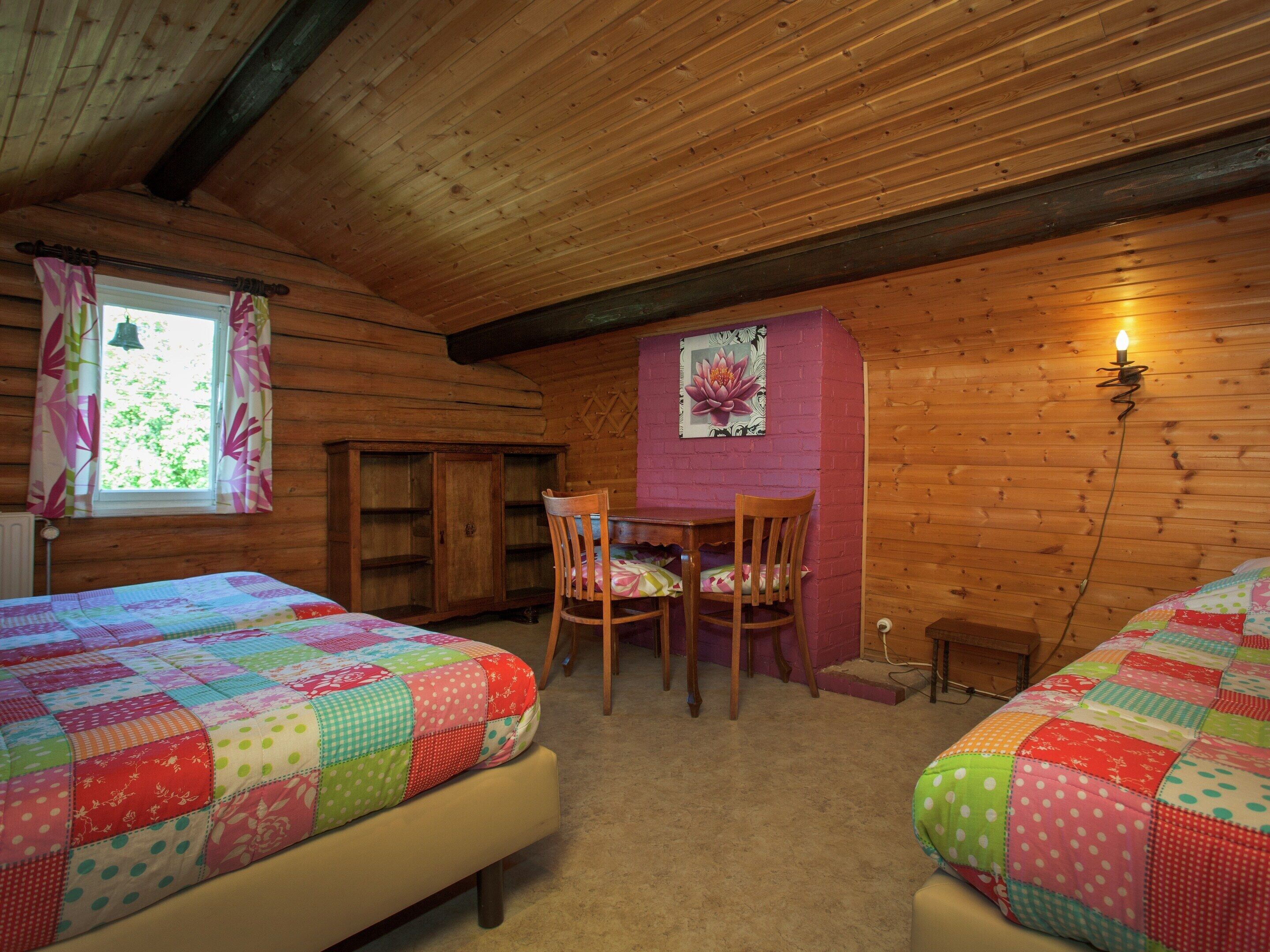 A cozy cabin room with two beds, a wooden desk, and a window with curtains.