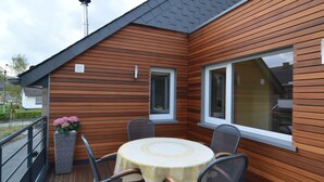 A wooden deck with a round table and chairs, a potted plant, and a window. - A Holiday Home Ideal for Families and for Discovering the Ardennes (Waimes)