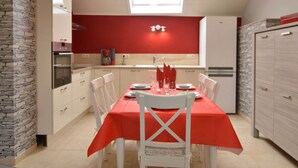 A compact kitchen with a dining area, featuring a red tablecloth, white chairs, and a stone accent wall. - A Holiday Home Ideal for Families and for Discovering the Ardennes (Waimes)