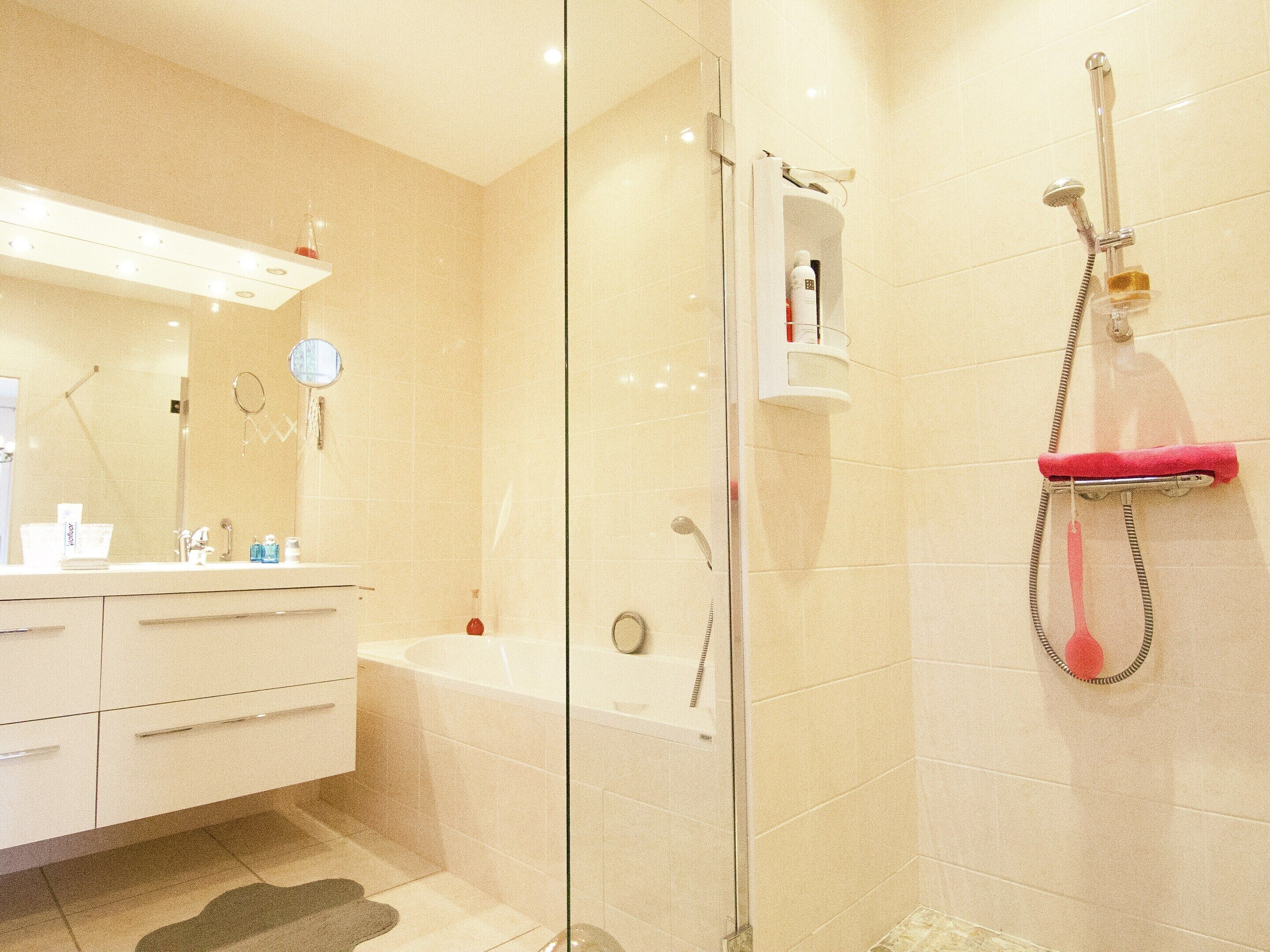 A modern bathroom with a glass shower enclosure, a white bathtub, and a vanity with a mirror and toiletries.