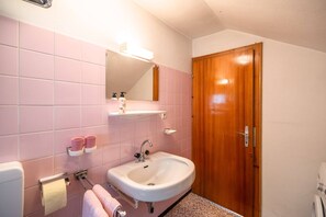 A bathroom with pink tiles, a white sink, a mirror, a wooden door, and a toilet. - Cozy Chalet in Obsteig With Terrace (Mieming)
