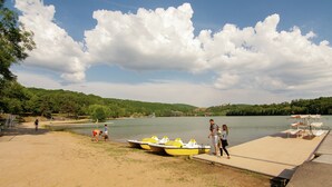 A lakeside dock with yellow boats, a sandy shore, and a forested hill in the background. - Cozy Garden Retreat Malemort (Malemort-sur-Correze)