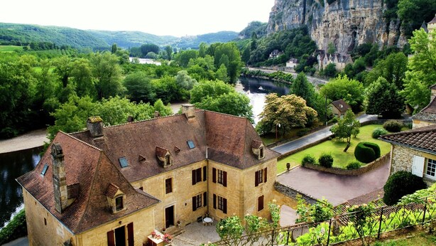 A historic stone building with a courtyard, surrounded by lush greenery and a river. - Cozy Garden Retreat Malemort (Malemort-sur-Correze)