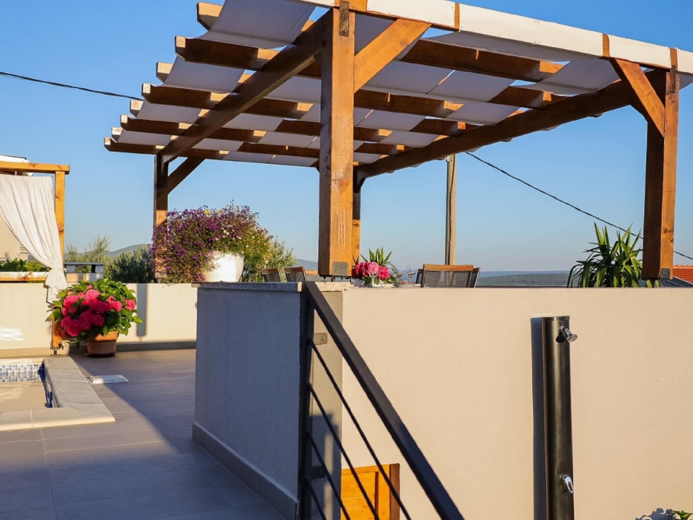 A covered outdoor area with a pergola, potted plants, and a view of the sea.
