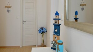 A hallway with a white door, a small blue lighthouse decoration, a vase with blue flowers, and a mirror reflecting the lighthouse. - Holiday Home With Private Swimming Pool (Jasenice)