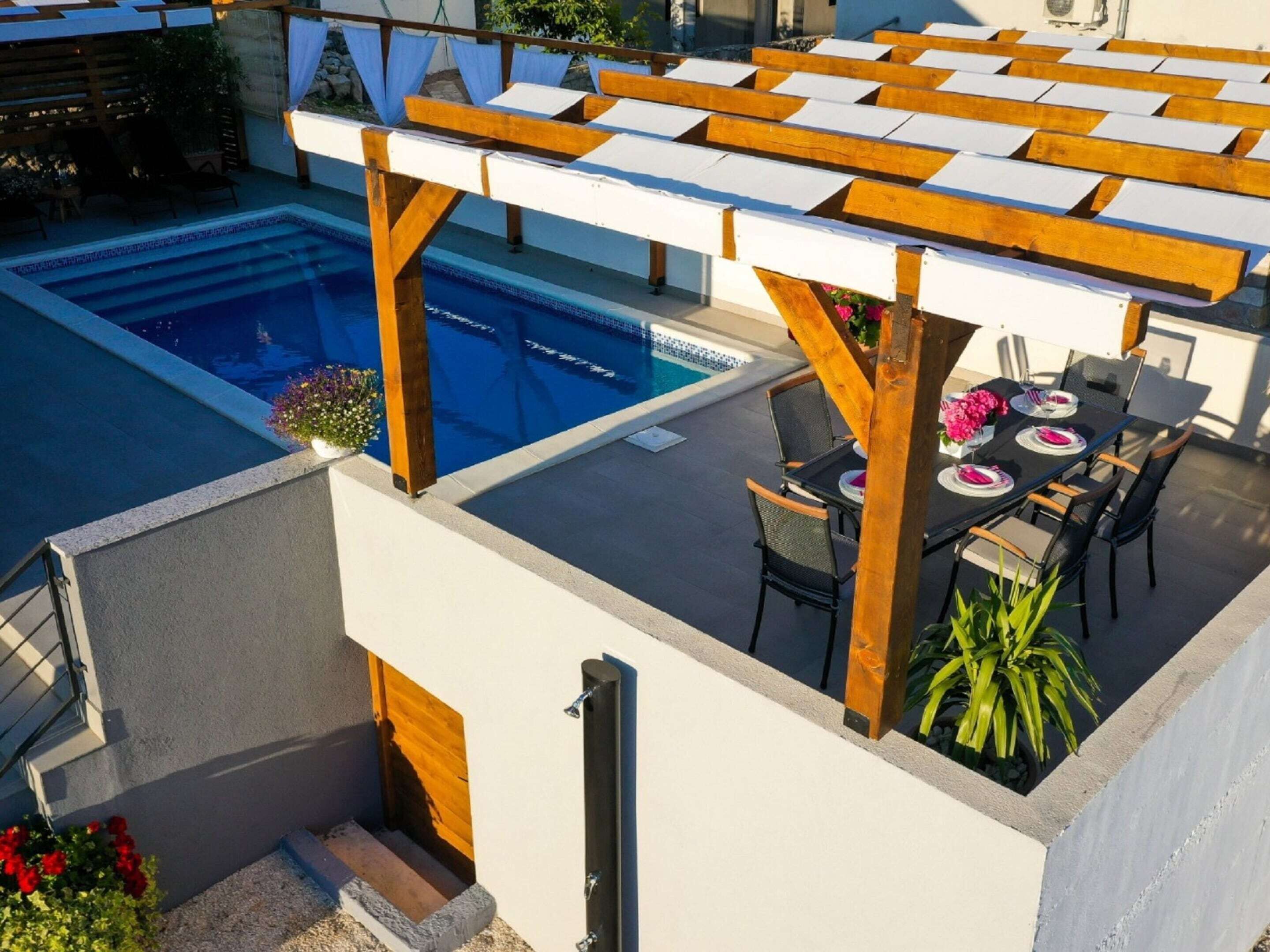 A rooftop pool area with a pergola, outdoor seating, and a view of the pool.