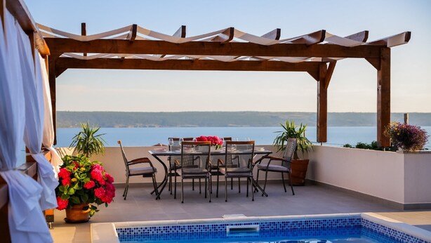 A poolside area with a pergola, a dining table with chairs, and a view of the sea. - Holiday Home With Private Swimming Pool (Jasenice)