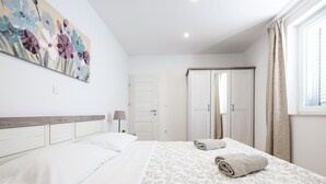 A hotel room with a bed, a nightstand, a lamp, a painting on the wall, and a window with curtains. - Holiday Home With Private Swimming Pool (Jasenice)