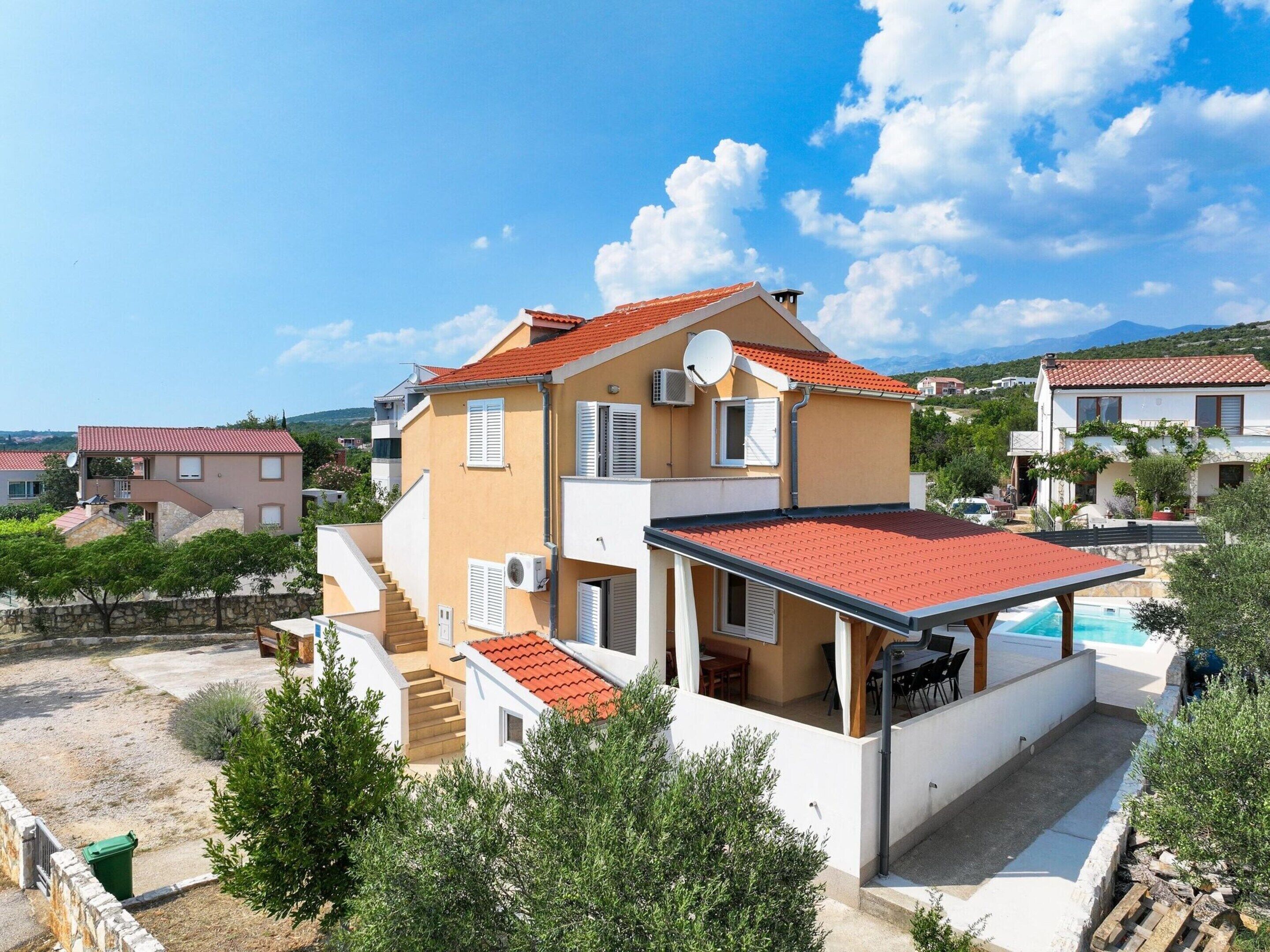 A two-story house with a red-tiled roof, a balcony, and a swimming pool.