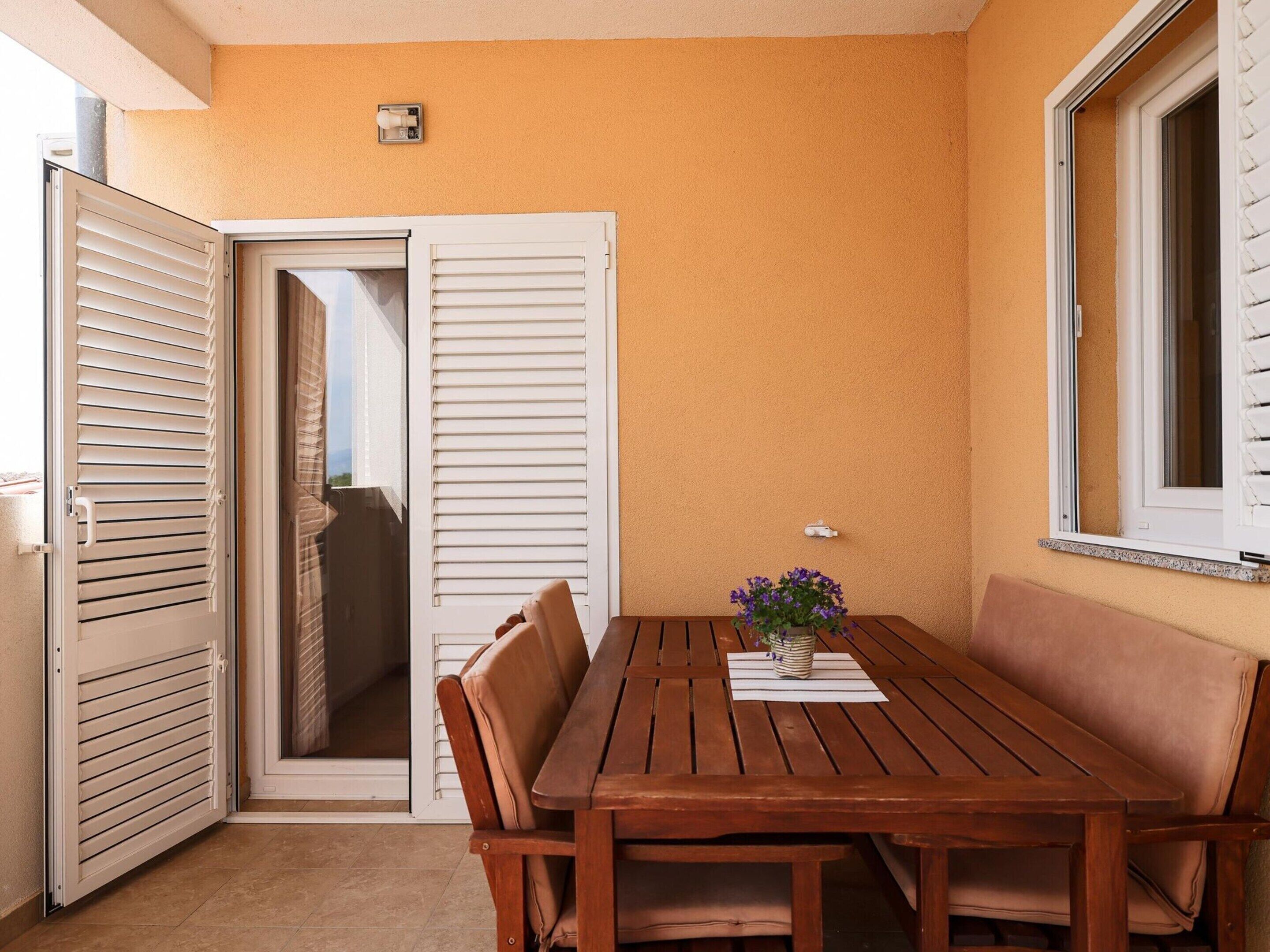 Una mesa de madera con cuatro sillas, una planta en maceta y una ventana con persianas.