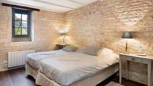 Ein Schlafzimmer mit Steingemäuer, einem Doppelbett, zwei Nachttischen mit Lampen und einem Fenster mit Aussicht.