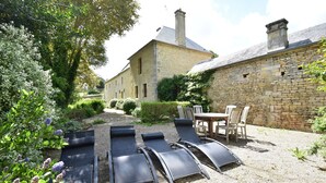Ein Garten mit Liegestühlen und einem Tisch mit Stühlen, umgeben von Steinmauern und Grünpflanzen.