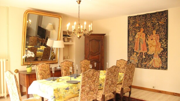 Ein Esszimmer mit einem für sechs Personen gedeckten Tisch, umgeben von stuhlierten Sesseln mit Blumenmuster, einer Kristallleuchter, einem großen Spiegel und einem Wandteppich.