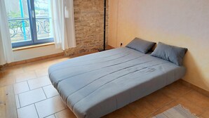 Un dormitori amb llit, finestra amb cortines, paret de pedra i làmpada de peu.
