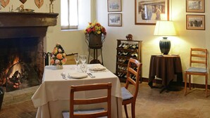 Un coin repas avec une cheminée, des chaises en bois, une table dressée pour deux personnes et un meuble à vin.