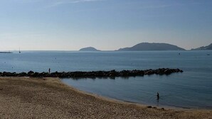 Une plage avec une digue rocheuse, une mer calme et des collines à l’horizon.