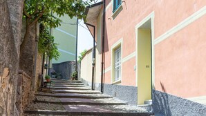 Une ruelle étroite pavée de pierres, avec des marches menant à un bâtiment doté d’une porte jaune et d’une fenêtre grillagée.