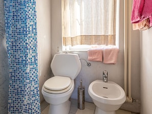Casa de banho com sanita, bidé e janela com cortinas.
