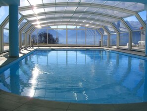 An indoor swimming pool with a glass ceiling, clear blue water, and a view of mountains. - Belvilla by OYO Villa Stenico (Stenico)