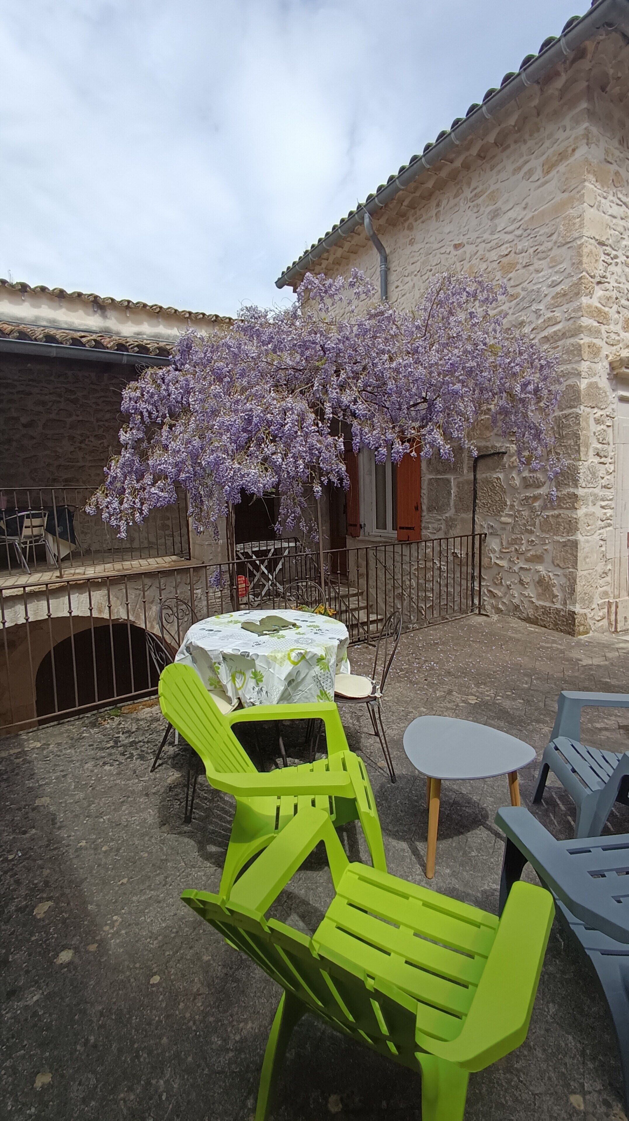 An outdoor seating area with a table and chairs, a stone building, and purple flowering vines.