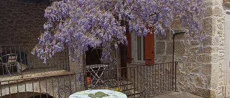 An outdoor seating area with a table and chairs, a stone building, and purple flowering vines.