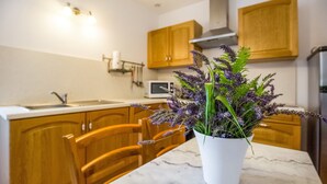 A kitchen with wooden cabinets, a white countertop, a microwave, and a potted plant with purple flowers. - Montclus Charm: Views & Calm (Montclus)