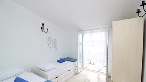 A bedroom with two beds, a sliding glass door to the balcony, a bedside table with a lamp, and a wall-mounted light fixture. - Apartment in Seline by the Sea (Starigrad)