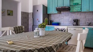 A compact kitchen with teal cabinets, a refrigerator, a coffee maker, and a dining table with a plaid tablecloth. - Apartment in Seline by the Sea (Starigrad)
