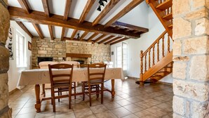 Un comedor con una mesa dispuesta para cuatro personas, sillas de madera, una pared de piedra y una escalera de madera.
