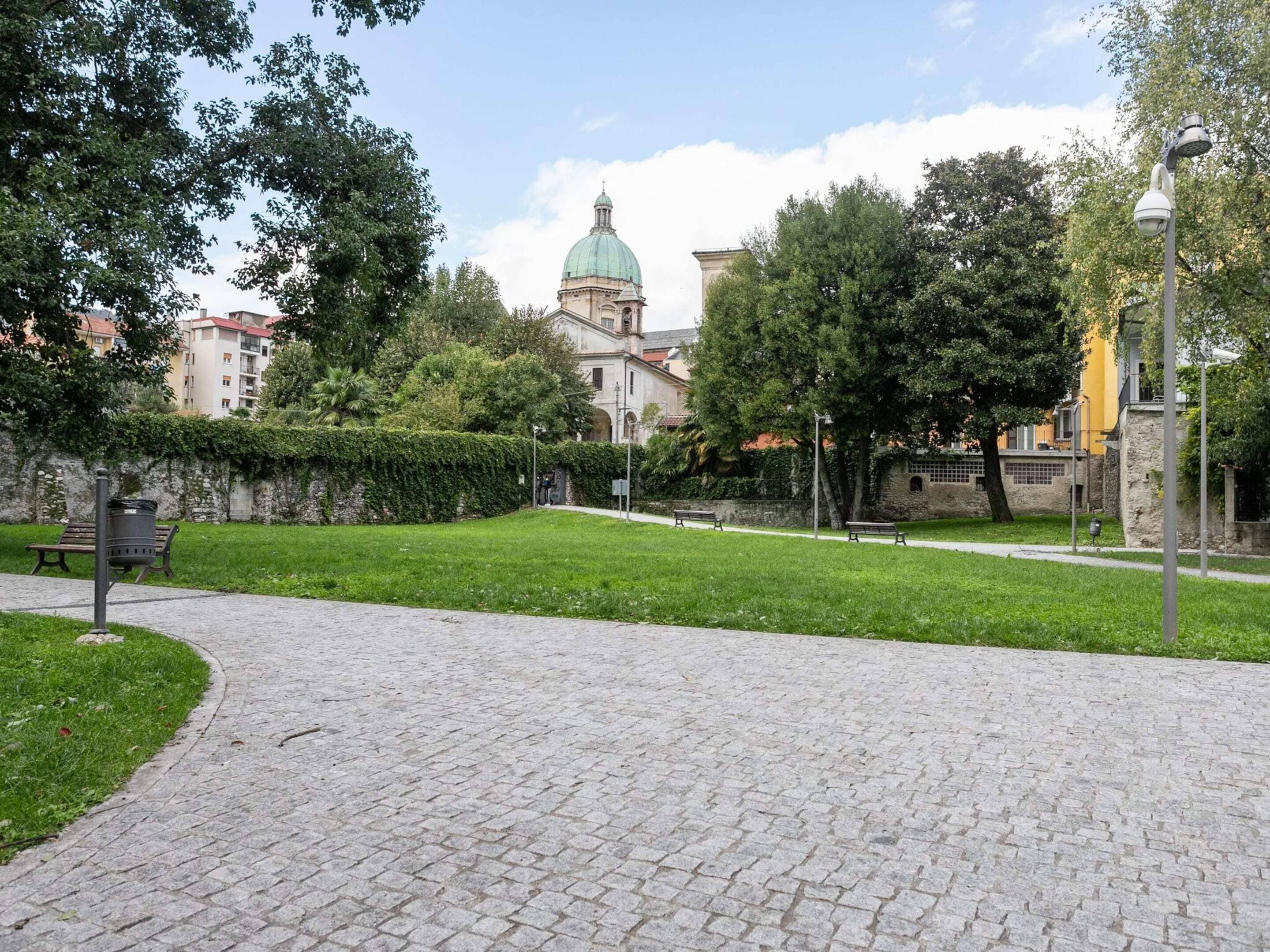 Un sendero pavimentado en un parque con bancos y césped verde.