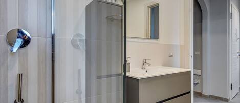 Ein modernes Badezimmer mit begehbarer Dusche, einem großen Spiegel und einem Waschtisch.