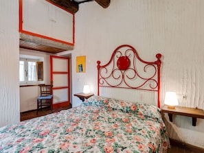 A bedroom with a floral bedspread, a red metal headboard, a wooden nightstand with a lamp, and a window with curtains. - Idyllic Retreat With Shared Pool (San Marcello Piteglio)