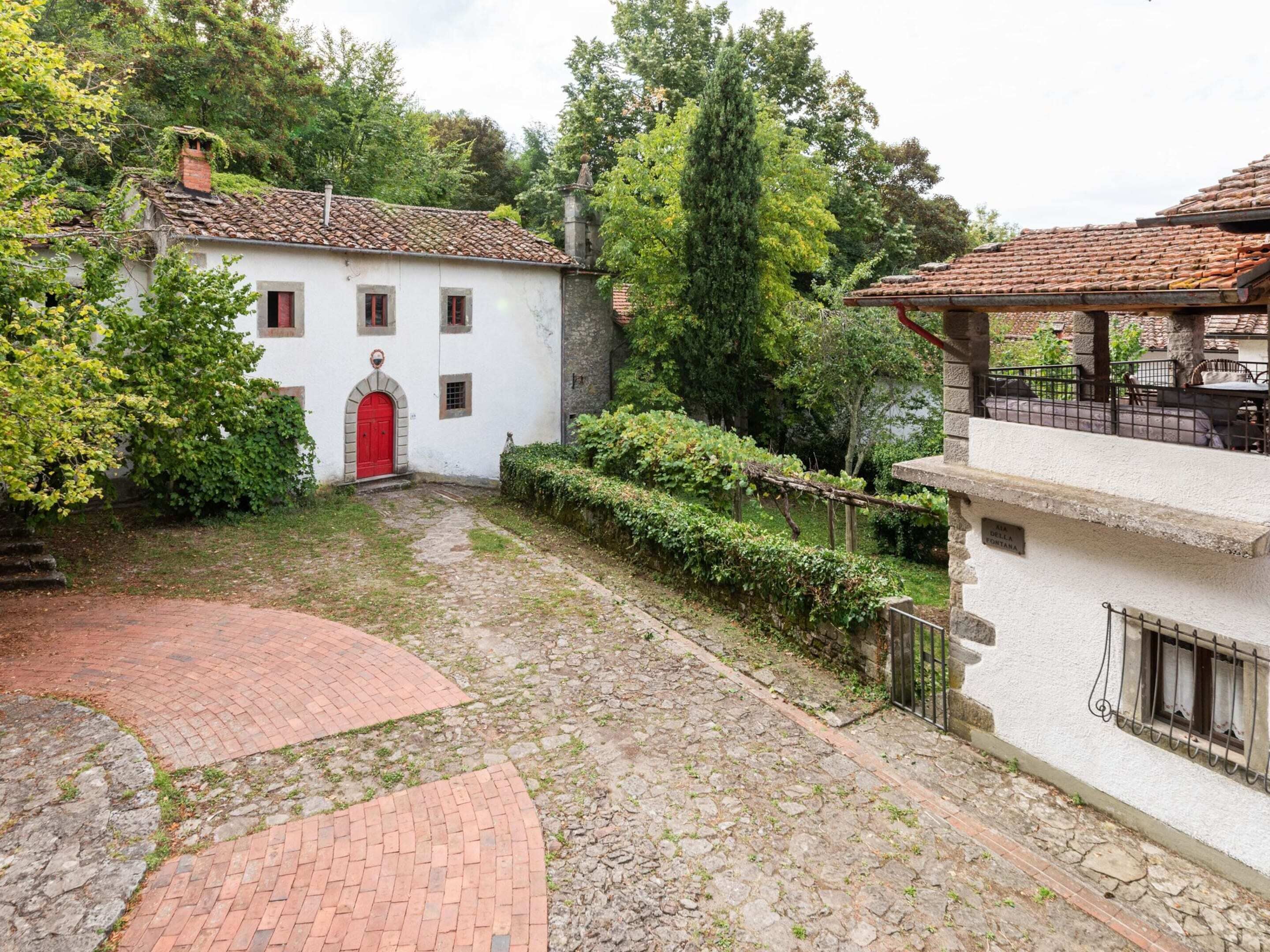 A courtyard with a red door, stone pathway, and white building with a tiled roof.