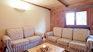 A cozy living room with two striped sofas, a wooden coffee table with a candle, and a brick wall with a window. - Exquisite Villa in Cesena With Sauna (Cesena)
