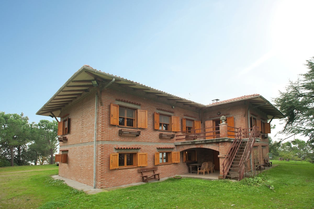 A two-story brick house with wooden shutters, a balcony, and a staircase leading to an upper level.
