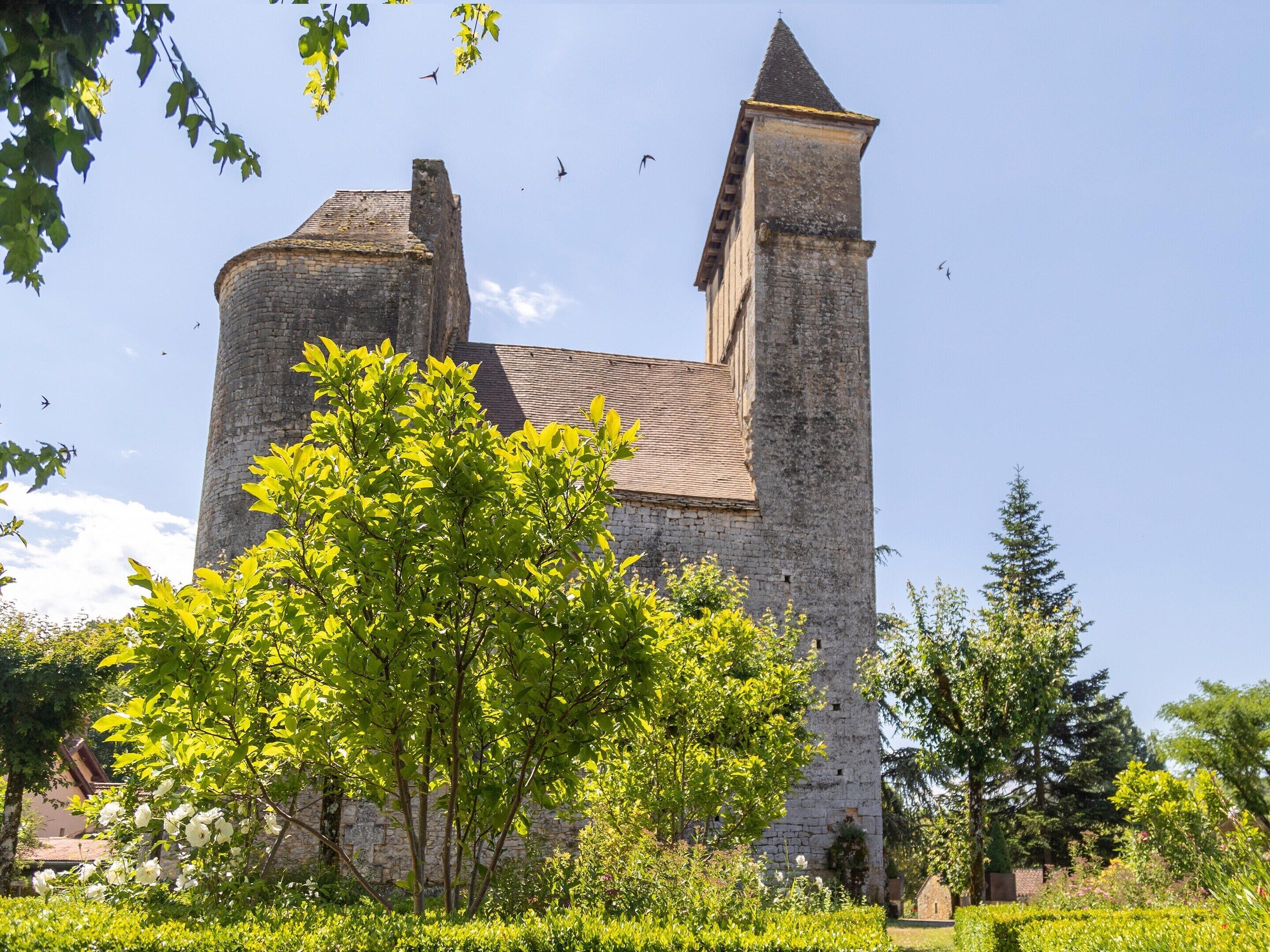 A historic stone tower with a conical roof, surrounded by lush greenery and a clear sky.