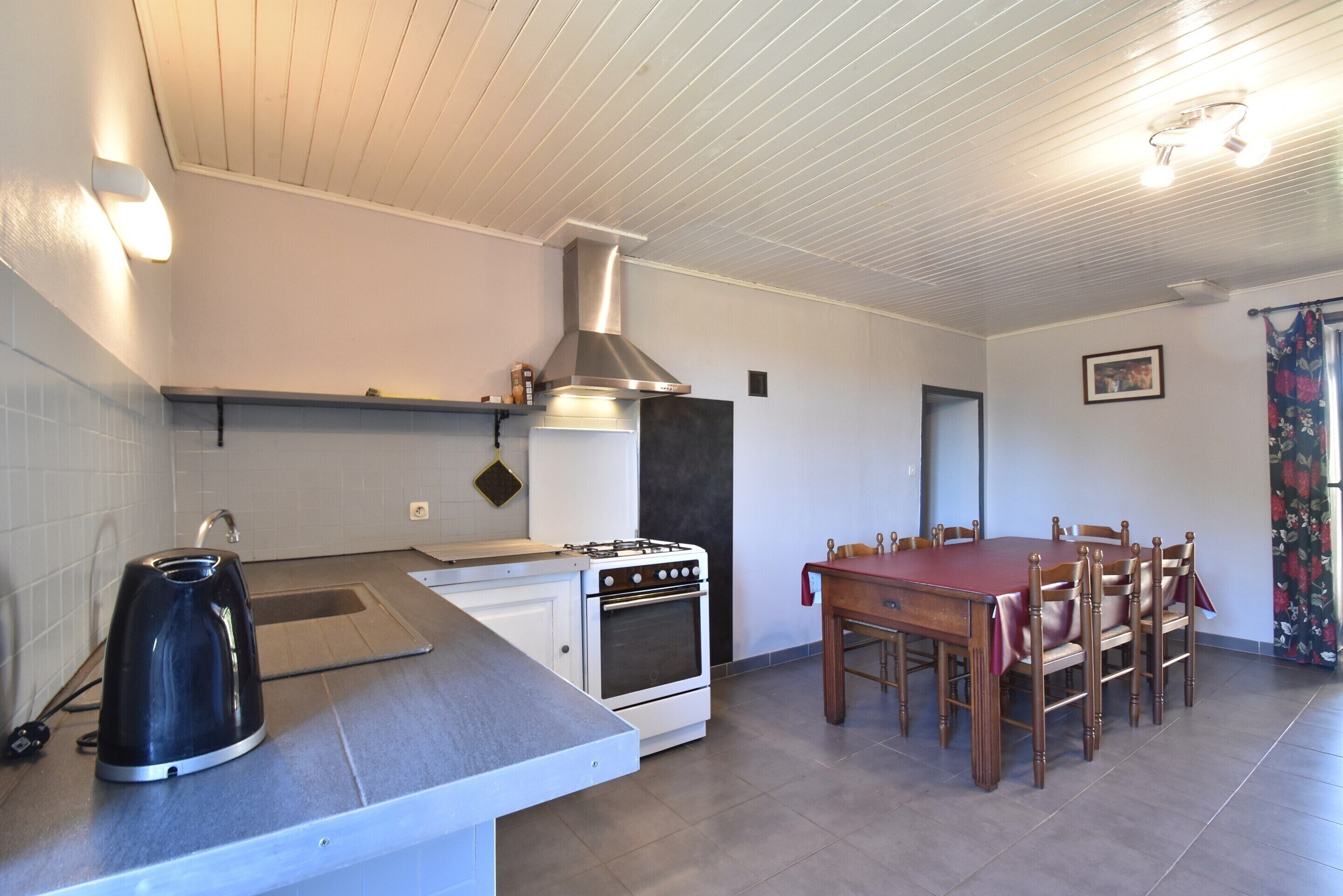 A kitchen with a stove, oven, and kettle, a dining table with chairs, and a ceiling with recessed lighting.