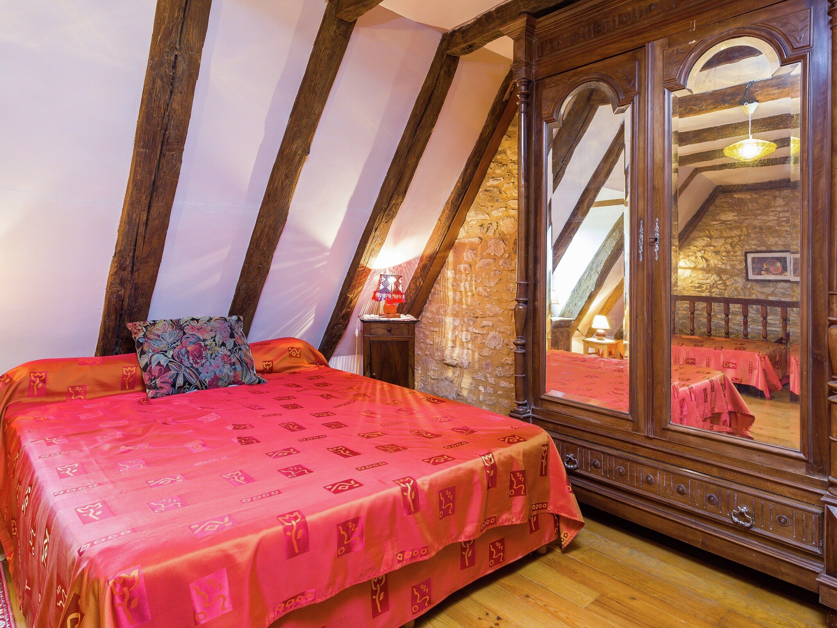 Un dormitorio con cama, armario de madera, pared de piedra y techo inclinado.