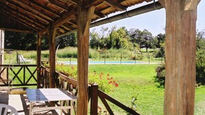 A wooden deck with a table and chairs, overlooking a grassy area with a pool and trees. - Comfortable Holiday Home With Private Pool (Besse)