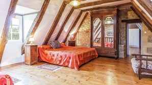 A bedroom with a sloped ceiling, wooden beams, a bed with a patterned bedspread, a nightstand, a lamp, and a view through a window. - Comfortable Holiday Home With Private Pool (Besse)