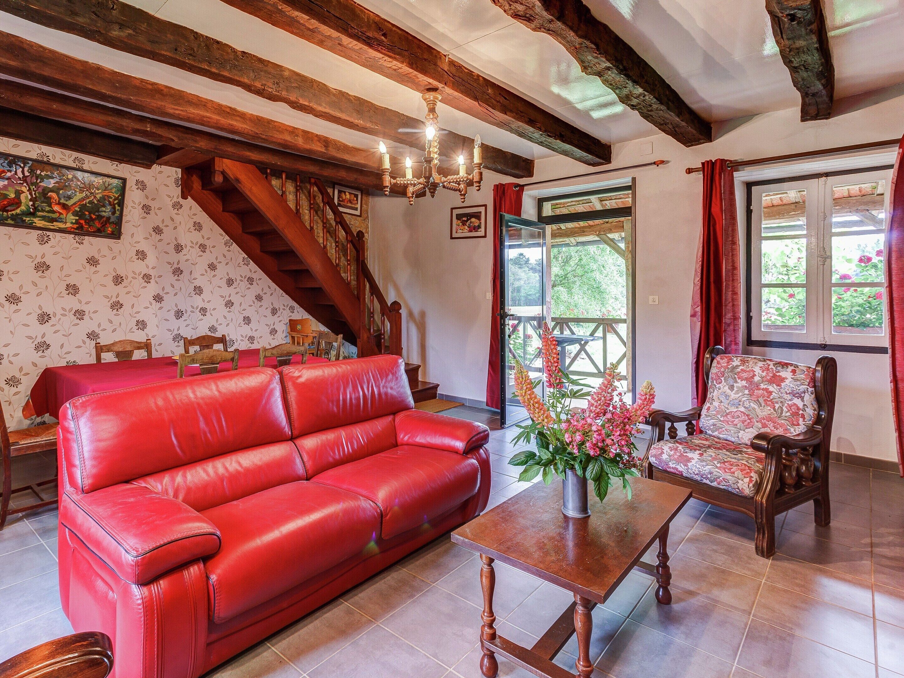 Una habitación con un sofá de cuero rojo, una mesa de madera con un jarrón de flores, una silla de madera y una escalera, además de techo de madera.